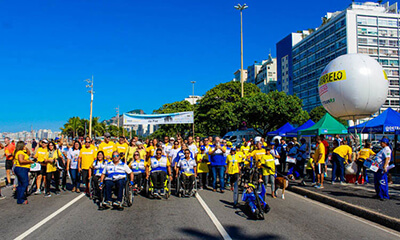 Várias pessoas de camisa amarela e alguns cadeirantes posam para foto na orla de Copacabana em prol da campanha Maio Amarelo.