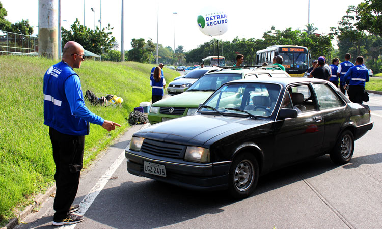 Agente do Detran Seguro fiscalizando um veículo (chevette) preto