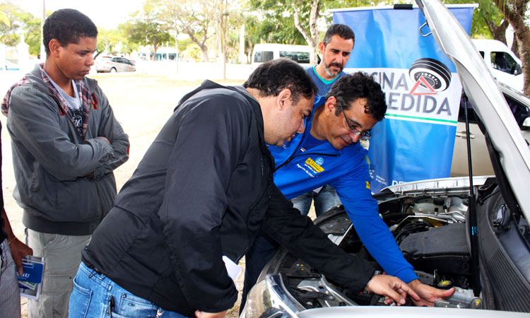 Um instrutor demonstrando a mecânica do carro para três alunos 