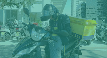 Motofretista parado na calçada acessa o celular para verificar a sua rota de entrega.