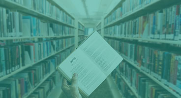 mão segurando um livro aberto entre duas estantes cheias de livros.